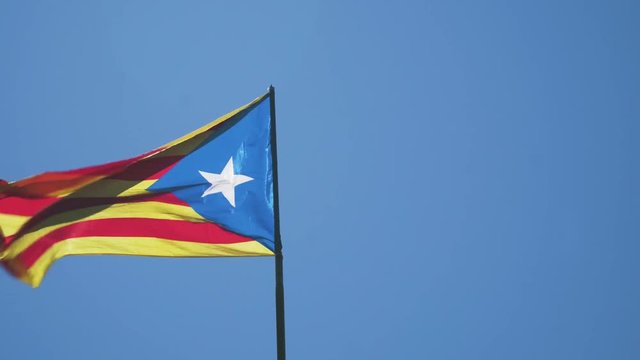 A flag of the Republic of Catalonia is waving because of a strong wind. The colors of the unofficial independence flag are red, yellow and blue, with a white star in the middle.