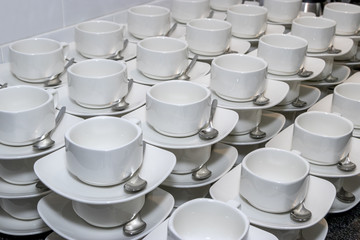 Smooth rows of white tea cups with spoons on a table in a restaurant