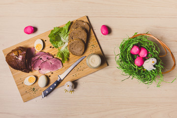 Smoked ham, eggs and bread on wooden board with spices. Easter decorations. Top view.