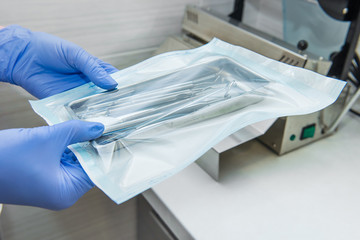 Close up dentist assistant's hands holding packaged with vacuum packing machine medical instruments...