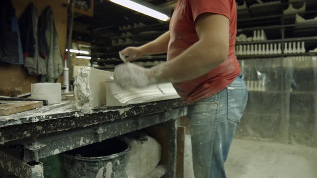 Worker made a part of gypsum cornice. Specialist separating ready part of cornice from gypsum at manufacture. Molding a cornice at manufactory.