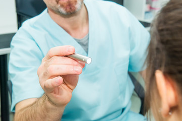 Close up doctor testing reflexes of the eye of young woman using a lamp in medical clinic....