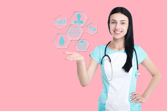 Woman doctor isolated on a clinic background raise a hologram medical icons on hand. Concept: medicine, innovative medical technology, healthcare.