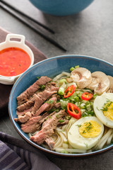 Asian ramen soup with beef, egg, chives and mushrooms in bowl.