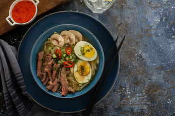 Asian ramen soup with beef, egg, chives, mushrooms in bowl on dark background. Top view
