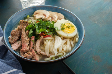 Asian ramen soup with beef, egg, chives and mushrooms in bowl.