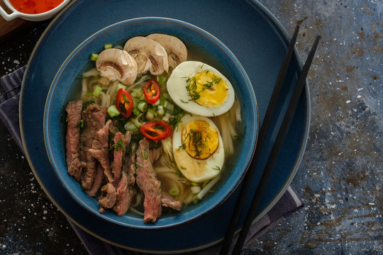 Asian ramen soup with beef, egg, chives, mushrooms in bowl on dark background.