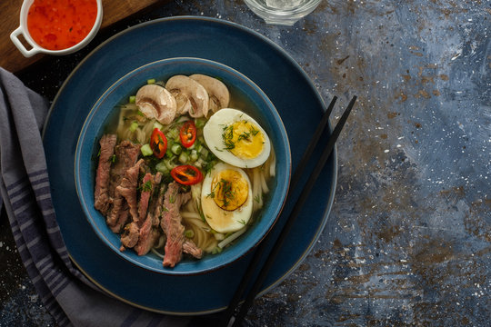 Asian ramen soup with beef, egg, chives, mushrooms in bowl on dark background. Copyspace. Top view