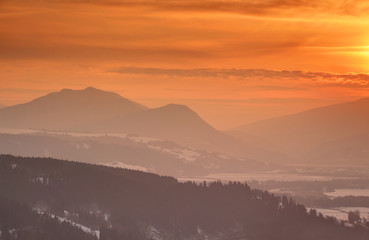 Glowing orange sunlight over misty silhouettes of Sip peak of Velka Fatra and Kuzminovo Oravska Magura mountain ranges at sunset, Carpathians Dolny Kubin Orava and Liptov Slovakia Central Europe