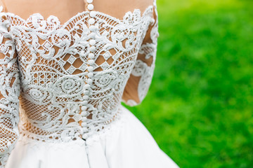 Beautiful lace on the back of the bride on the background of green grass