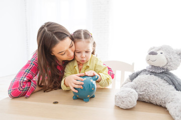 Mother and her child daughter putting coin to piggy bank