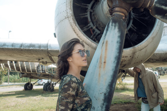 Girl in camouflage shirt near propeller and turbine of old plane on sunny day. Military woman, pilot on aerodrome. Couple on excursion at aviation museum, husband tired of walking. Air forces concept.