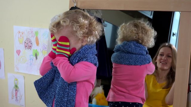 Playful little girl and her mother playing near mirror
