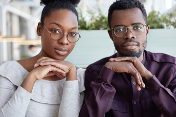 Teamwork and cooperation concept. Successful African American female and male colleagues sit close to each other, wears spectacles, work on common project. Business partners have meeting in cafe