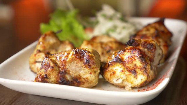 Close of roasted meat lying on a white plate with greens on a table in slow motion, 4k, steam from hot meat