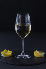 a glass of white wine on a black table with a fruit dessert