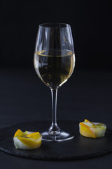 a glass of white wine on a black table with a fruit dessert on a diagonally line