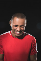 Close up waist up portrait of young african guy in red t-shirt. He is very sincerely laughing with closed eyes. Isolated on black background