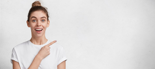 Happy delighted young female model with amazed expression, hair bun, dressed casually, isolated...