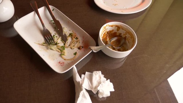 Empty dirty white plates with fork, spoon and waste food after eaten on table, 4k