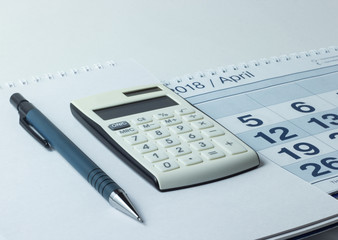 Calculator and pen on calendar background