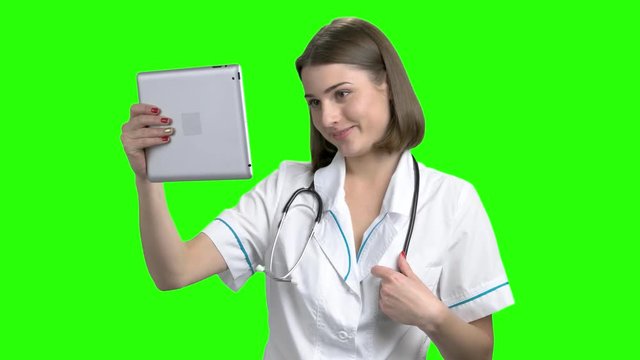 Young female doctor having online coversation on tablet computer. Green screen hromakey background for keying.