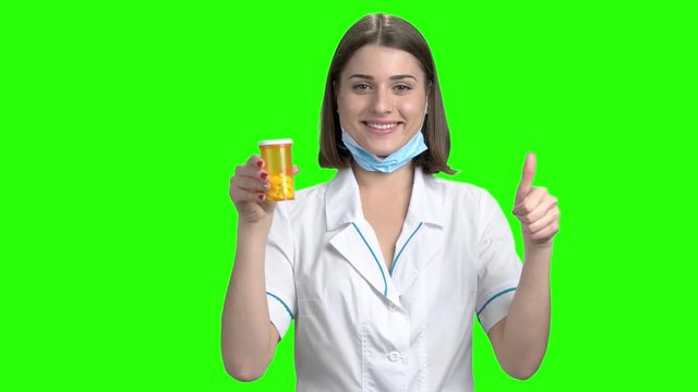 Young female doctor recommed pills. Yellow can of pills advertising, thumb up. Green screen hromakey background for keying.