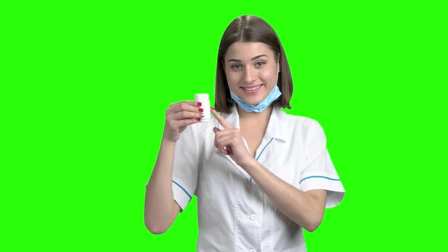 White can of pills promotion, thumb up. Young brunette smiling female doctor recommed pills. Green screen hromakey background for keying.