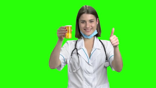 Young female doctor advertising yellow can of pills. Green screen hromakey background for keying.