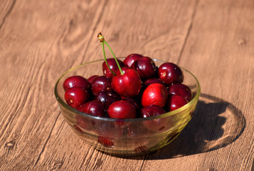Berries of a sweet cherry in a glass bowl on a wooden background. Ripe red sweet cherry