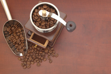 Manual coffee grinder with shovel and roasted coffee beans on  table