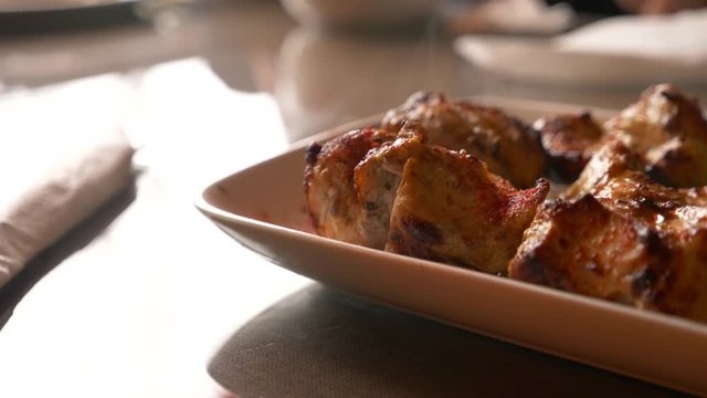 Close of roasted meat lying on a white plate with greens on a table in slow motion, 4k, steam from hot meat