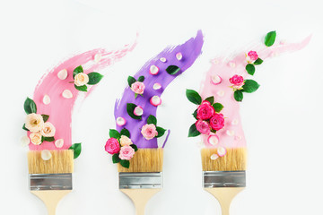 Paintbrushes with taces of pink and violet shades, roses and petals, on a white background with copy space. Painting spring creative flat lay. Home decoration concept.