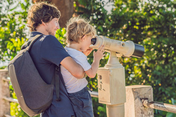 Father and son are looking at Coin-operated binoculars at the sea