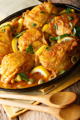 Stewed chicken with salted lemons, onions and green olives closeup on a plate. vertical