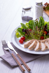 Chicken breast salad on a white plate with spoon and knife