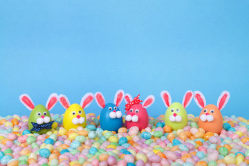 Craft Easter Bunnies made from plastic eggs standing in pastel jelly beans with a light blue background. Fun Easter line up with copy space