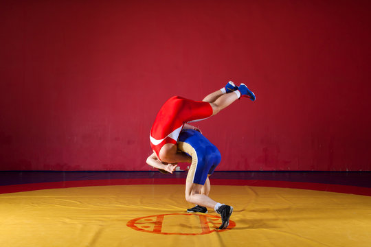 Two greco-roman  wrestlers in red and blue uniform wrestling   on a yellow wrestling carpet in the gym