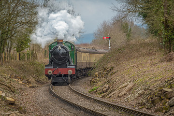 A steam train appears from around a bend heading straight towards the camera. The steam locomotive is complete with carriages and smoking 