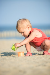 Baby playing on the sandy beach near the sea. Cute little girl in red dress with sand on tropical beach. Ocean coast.