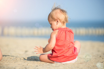 Fototapeta na wymiar Baby playing on the sandy beach near the sea. Cute little girl in red dress with sand on tropical beach. Ocean coast.