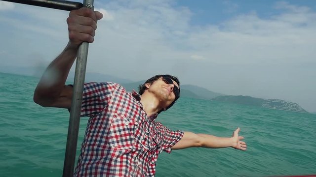 Happy young man in sunglasses enjoying sailing boat on sea raises hand and touches splashing water in slow motion. 1920x1080