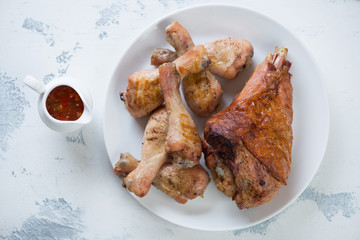 White plate with roasted turkey leg and chicken drumsticks on a white concrete background, horizontal shot, top view