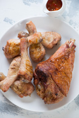 Above view of barbecued turkey and chicken legs on a white plate, vertical shot, closeup
