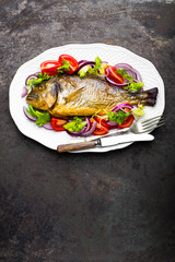 Baked fish dorado. Dorado fish oven baked and fresh vegetable salad on plate. Sea bream or dorada fish grilled and vegetable salad