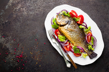 Baked fish dorado. Dorado fish oven baked and fresh vegetable salad on plate. Sea bream or dorada fish grilled and vegetable salad