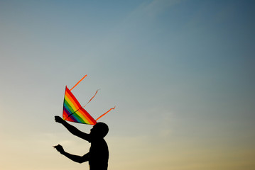 silhouette of active young man operating multicolor kite flying in air at summer sunset with copyspace