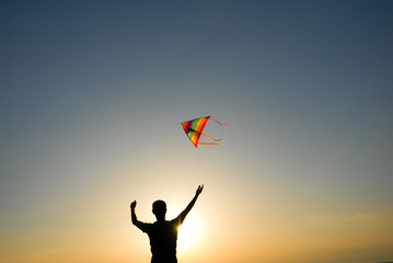 silhouette of healthy active young man holding colorful kite flying in blue sky at summer sunset