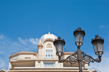 Fototapeta na wymiar Antique lamps on european street with baroque building and blue sky. Medieval architecture in Spain.Fasade of beautiful house with balcons.Card with sightseeng of europe.