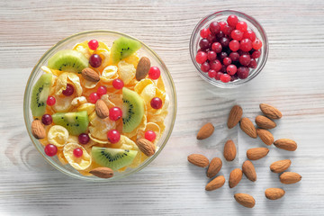 Two bowls with cornflakes, kiwi fruits, cranberries and scattered almonds on the light table. Concept of healthy breakfast.